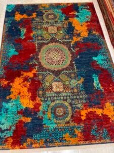 Azerbaijan Tappeti Milano Un tappeto colorato caratterizzato da un intricato motivo geometrico centrale con accenti astratti rossi, arancioni, verde acqua e blu lungo i bordi.