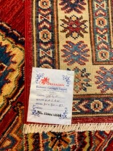 Azerbaijan Tappeti Milano Un tappeto decorato con un'etichetta di riparazione che riporta note scritte a mano in italiano e il nome dell'azienda, "Azerbaijan.