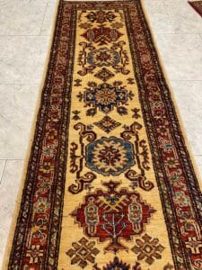 Azerbaijan Tappeti Milano Un tappeto da corridoio decorato con motivi geometrici in rosso, blu e beige su un pavimento piastrellato.