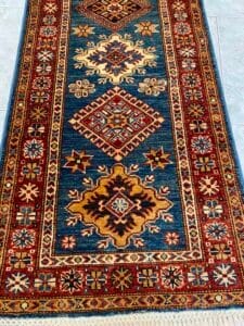 Azerbaijan Tappeti Milano Un tappeto colorato con disegni geometrici in blu, rosso, oro e crema.