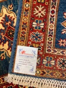 Azerbaijan Tappeti Milano Primo piano di un colorato tappeto intrecciato con etichetta attaccata, che mostra intricati motivi rossi, blu e arancioni.