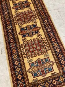 Azerbaijan Tappeti Milano Un tappeto con motivi geometrici in rosso, blu e beige su un pavimento piastrellato.