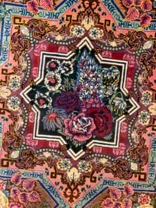 Azerbaijan Tappeti Milano Tappeto colorato con motivo floreale centrale e forme geometriche, caratterizzato da toni rosa, rossi e blu.