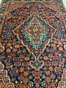 Azerbaijan Tappeti Milano Un tappeto orientale decorato con un medaglione centrale e intricati motivi floreali blu, rossi e beige.