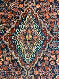 Azerbaijan Tappeti Milano Tappeto persiano decorato con motivi floreali e colori intensi di blu, rosso e crema; logo nell'angolo in alto a destra.