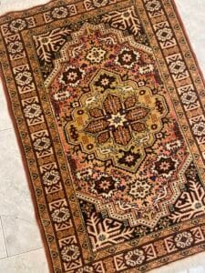 Azerbaijan Tappeti Milano Un tappeto orientale con motivi marroni, dorati e neri, caratterizzati da intricati disegni geometrici e floreali.