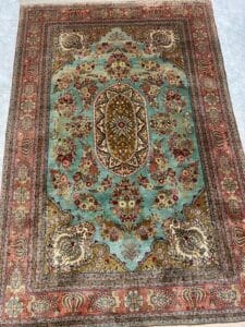 Azerbaijan Tappeti Milano Tappeto persiano decorato con medaglione ovale centrale e motivi floreali nei toni del rosso, oro e verde.