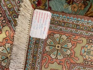 Azerbaijan Tappeti Milano Primo piano di un tappeto decorato con un'etichetta che riporta i dettagli del prodotto e un logo colorato in un angolo.