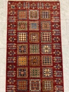 Azerbaijan Tappeti Milano Tappeto rettangolare rosso con motivi geometrici e floreali a quadrati arancioni, verdi, gialli e blu.