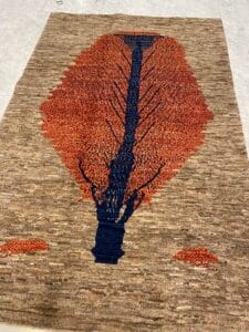 Azerbaijan Tappeti Milano Un tappeto tessuto a mano raffigurante un grande albero rosso-arancio con tronco blu su sfondo beige.