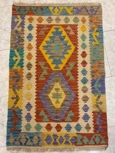 Azerbaijan Tappeti Milano Tappeto colorato con motivi geometrici, tra cui figure rosse, gialle, blu e verdi su sfondo beige.