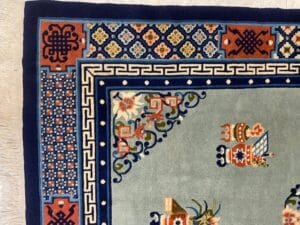 Azerbaijan Tappeti Milano Angolo di un tappeto decorato con motivi floreali e geometrici nei toni del blu, dell'arancione e del verde.