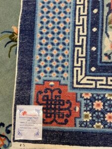 Azerbaijan Tappeti Milano Primo piano di un tappeto decorato con un'etichetta in un angolo e un logo colorato a forma di farfalla sopra.