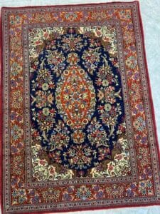 Azerbaijan Tappeti Milano Colorato tappeto in stile persiano con intricati motivi floreali nei toni del blu, rosso e crema, raffigurato su un pavimento piastrellato.