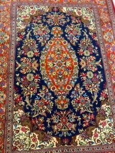 Azerbaijan Tappeti Milano Tappeto decorato in stile persiano con motivi floreali in rosso, blu, crema e oro e una farfalla colorata in un angolo.