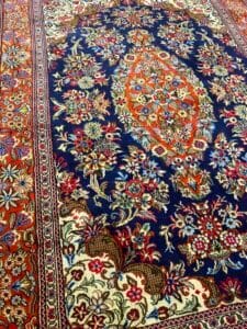 Azerbaijan Tappeti Milano Colorato tappeto persiano con intricati motivi floreali nei toni del blu, rosso, crema e arancione, parzialmente raffigurati in diagonale.