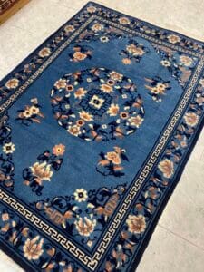Azerbaijan Tappeti Milano Tappeto blu in stile orientale con motivi floreali e geometrici su pavimento piastrellato di colore chiaro.