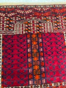Azerbaijan Tappeti Milano Un tappeto intrecciato colorato, decorato con motivi geometrici nei toni del rosso, dell'arancione e del blu navy.