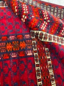 Azerbaijan Tappeti Milano Primo piano di un tappeto rosso intrecciato con disegni geometrici e decorativi nei toni dell'arancione, blu e bianco.